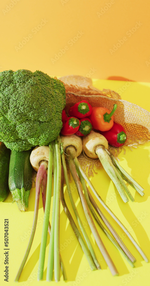 Vertical image of fresh vegetables with broccoli and peppers on yellow background