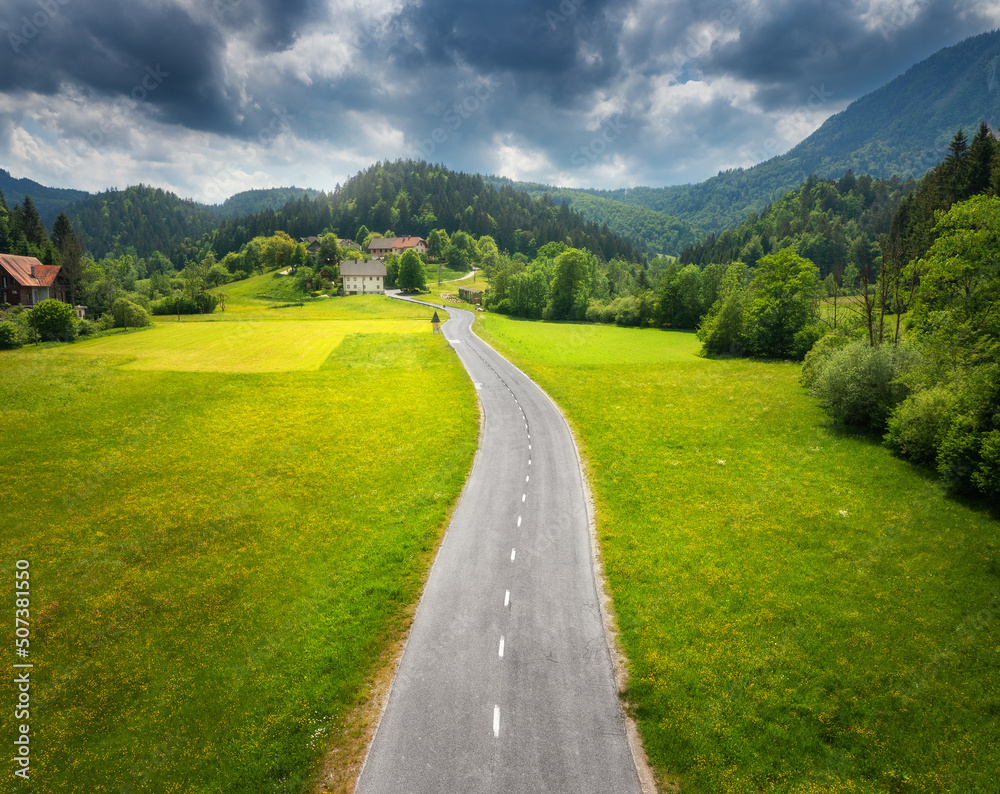 夏季日落时，绿色草地和山丘上的道路鸟瞰图。乡村道路的无人机俯视图