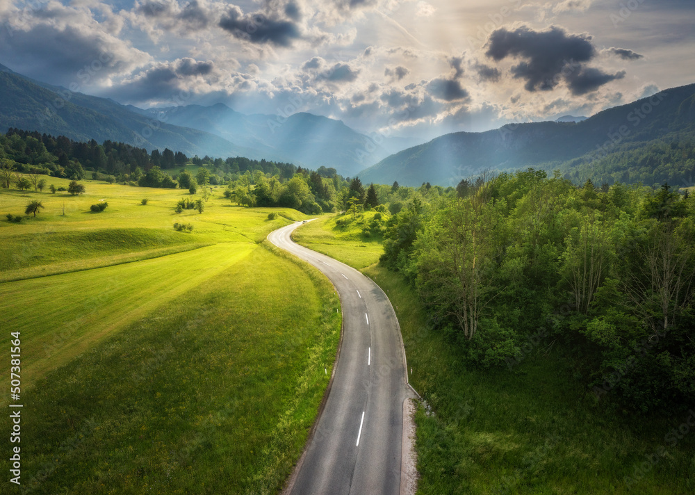 夏季日落时绿色草地上的道路鸟瞰图。无人机拍摄的山区乡村道路俯视图