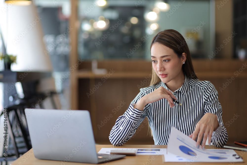 Business woman in office working with laptop and business finance documents.