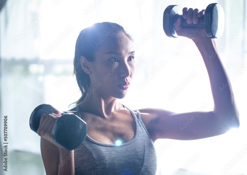 亚洲年轻女性在家做哑铃锻炼，锻炼手臂力量，运动型女性举重