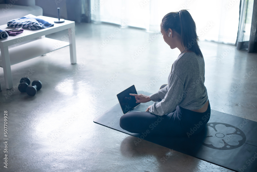 Sporty young Asian woman exercising at home, watching fitness video on Internet or having online fit