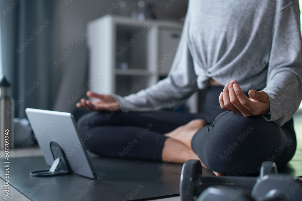 Sporty young Asian woman exercising at home, watching fitness video on Internet or having online fit