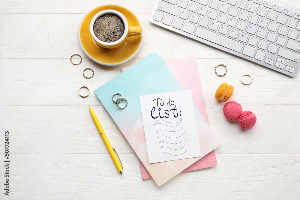 Notebook with blank to-do list, computer keyboard, coffee and macarons on white wooden background