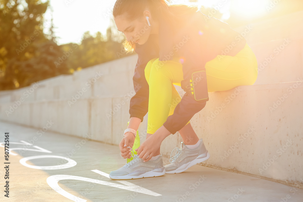 Sporty young woman tying shoelaces outdoors. Concept of 2022 goals