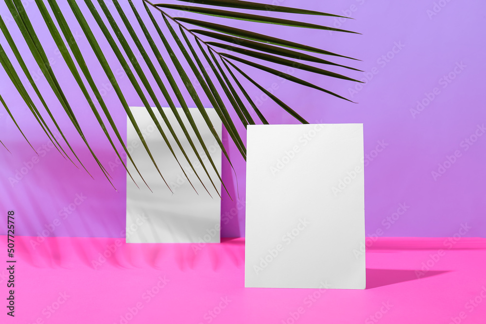 Blank paper sheets and palm leaf on color background