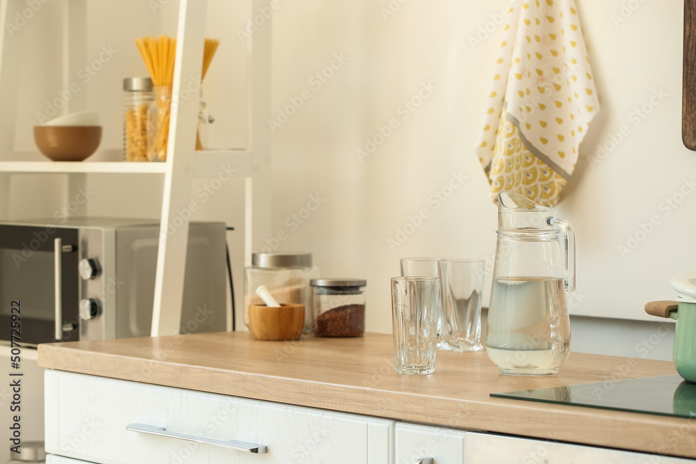 Jug with water and empty glass on counter in light kitchen