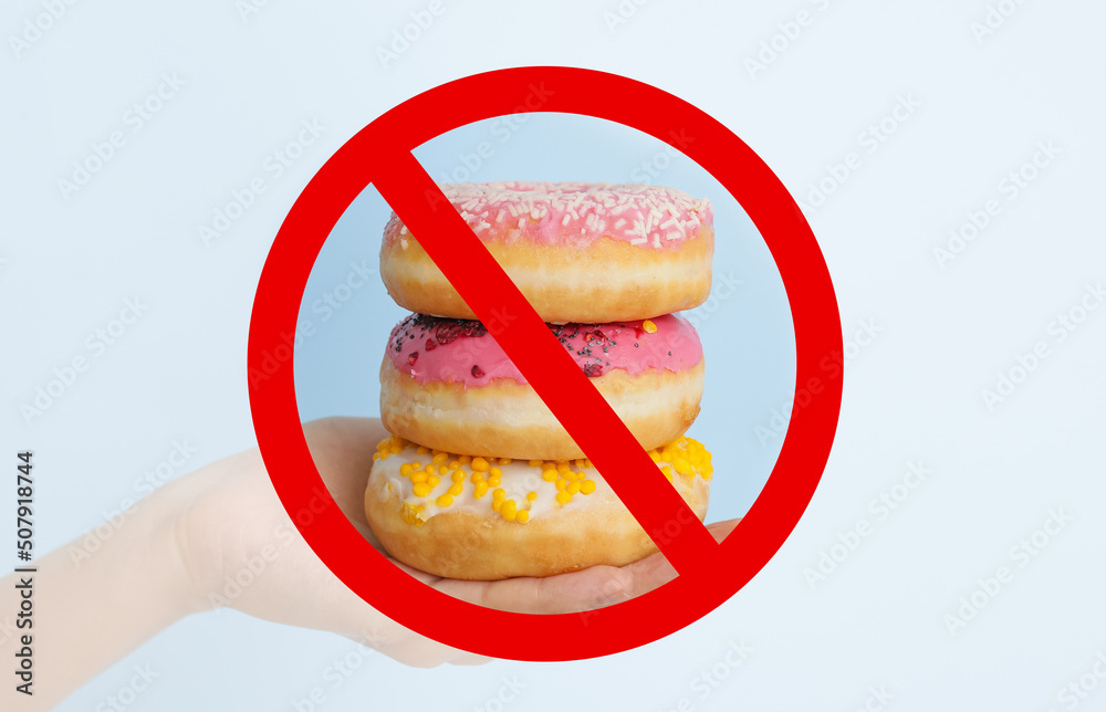 Hand with sweet donuts and prohibition sign on light background