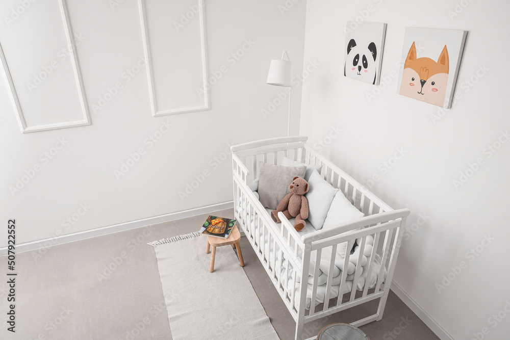 Interior of light nursery with baby crib, lamp and pictures