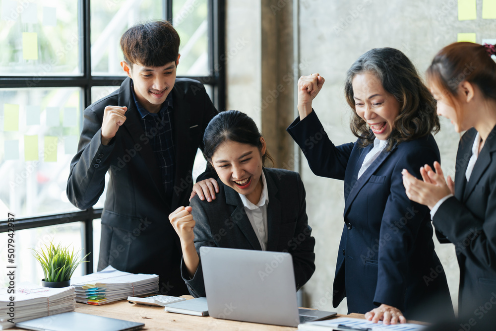 Celebrating success. Group happy asian business people in smart casual wear looking at the laptop an