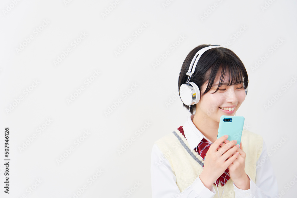 白背景でヘッドホンでスマホで音楽を聴く女子高生　コピースペースあり