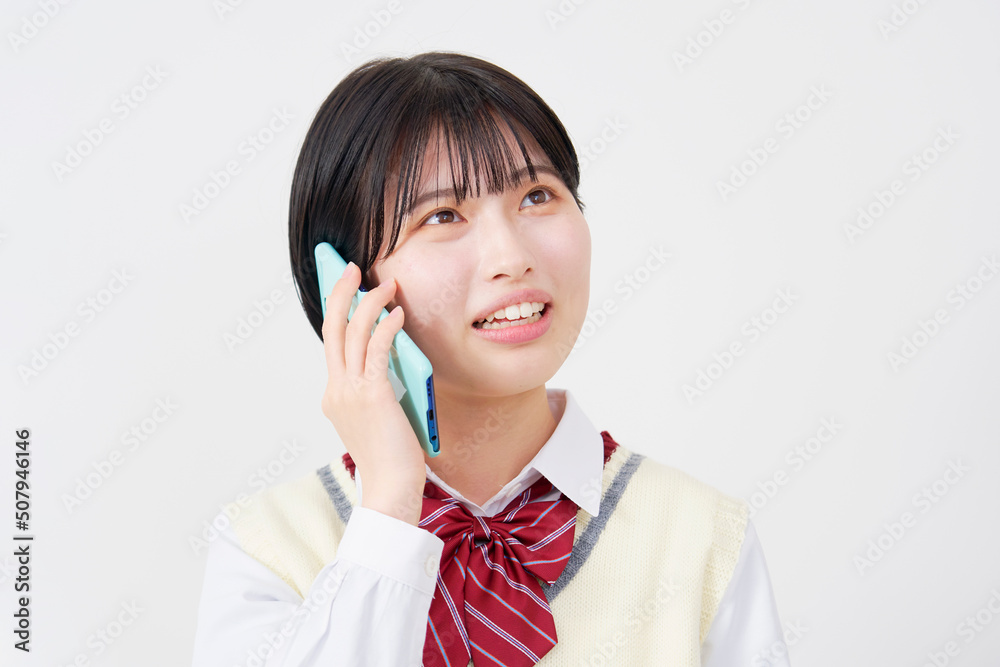 白背景で困った表情でスマホで電話をする女子高生