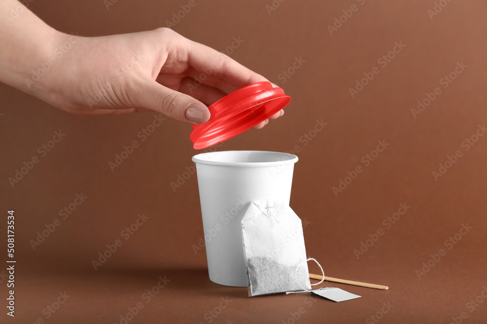 Female hand with takeaway paper cup of hot tea and bag on brown background