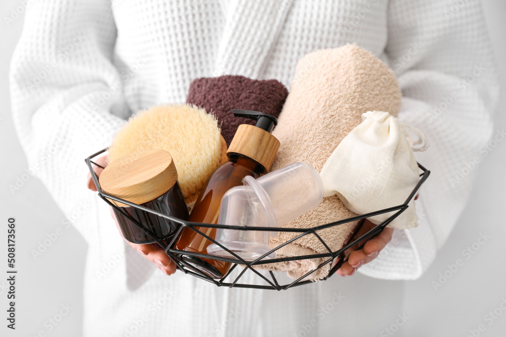 Woman holding basket with different bath supplies on light background, closeup