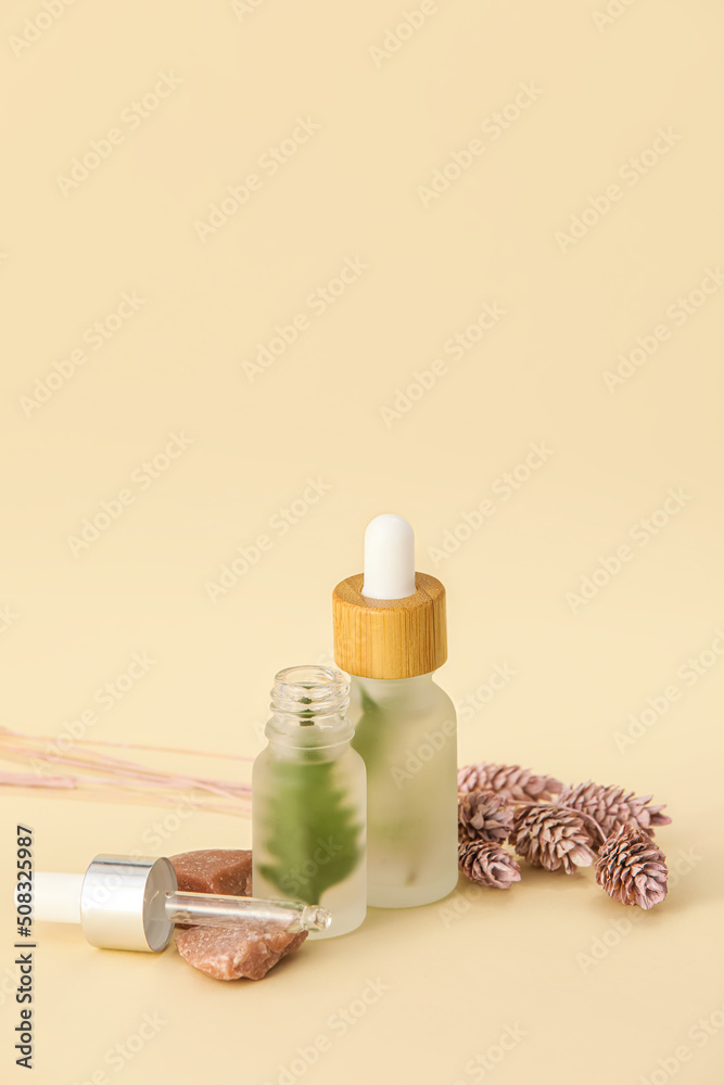 Bottles of natural serum and flowers on beige background