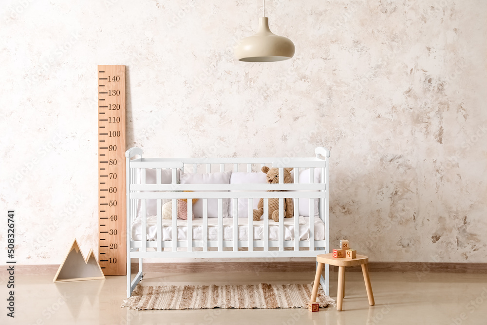 Interior of light nursery with baby crib, stadiometer and stool