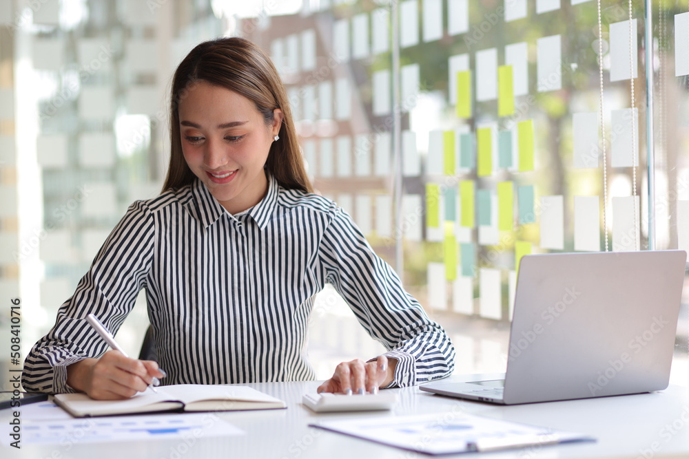 Businesswoman in the office working with financial data using calculator and writing make note with 