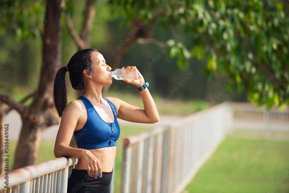 Asian woman in sport clothes  with smart watch on hands drinking water after workout at park