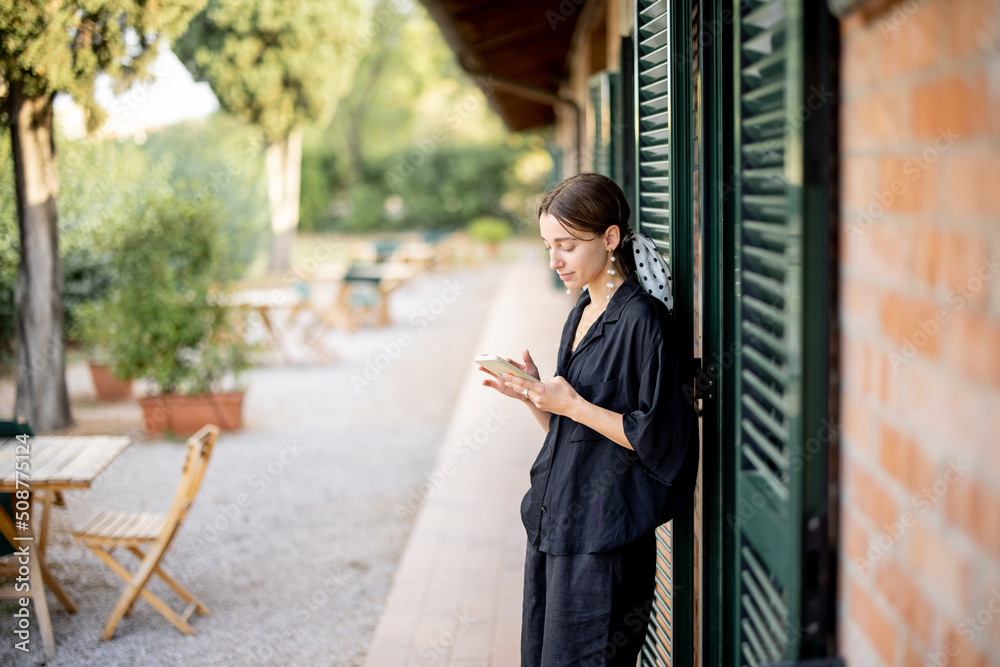 Young caucasian woman standing with smart phone in garden near hotel suit. Concept of weekend, rest 