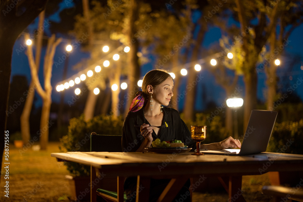 Caucasian woman watching something on laptop computer at evening time outdoors. Young woman sitting 