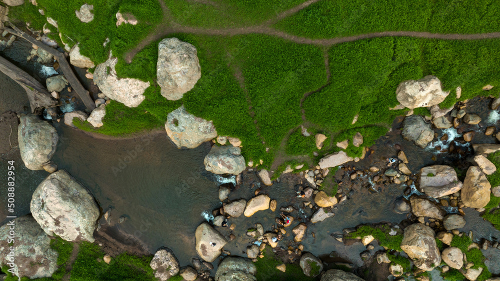 Aerial view of beautiful natural water stream  and green field of grass in the wild forest mountain 