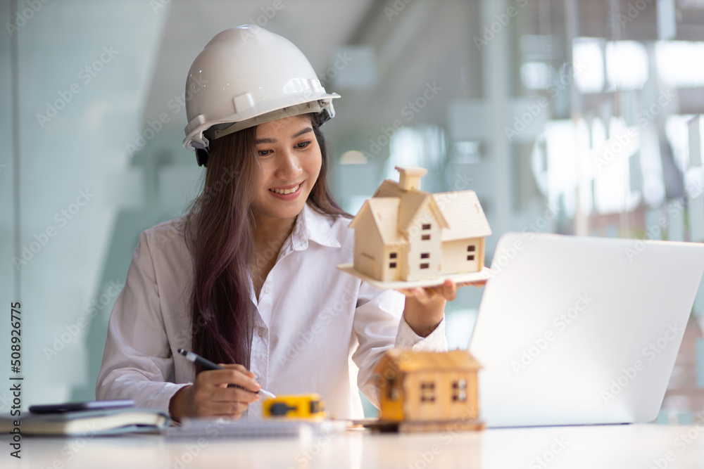 Female architect designer in an office working on a laptop is modeling a house and writing a housing