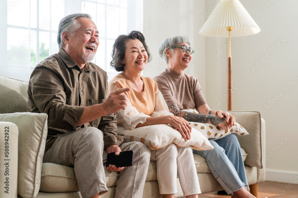 group of asian old senior male and female spending weekend time together sit on sofa couch watching 