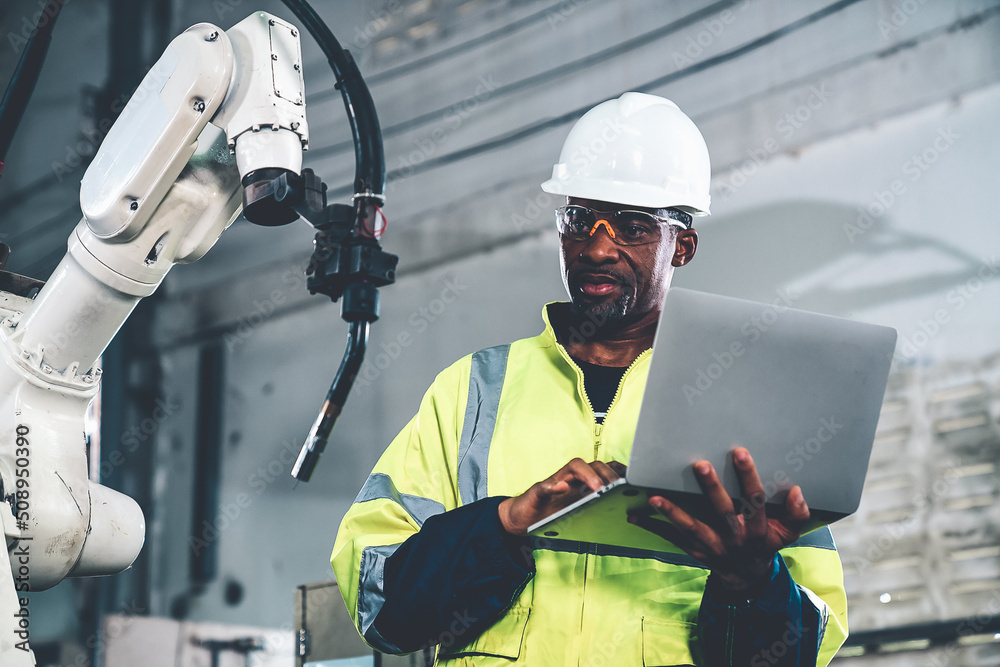 African American factory worker working with adept robotic arm in a workshop . Industry robot progra