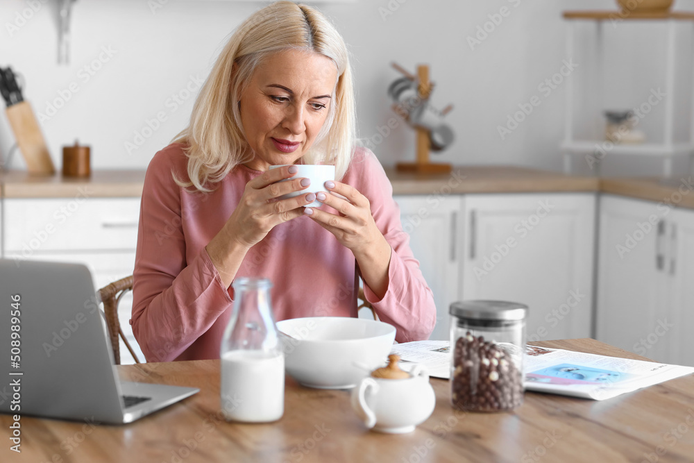 成熟女人在厨房喝咖啡看报纸的早晨