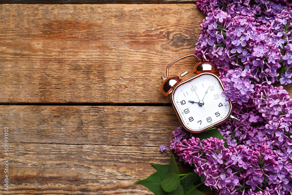 Purple lilac flowers with alarm clock on wooden background