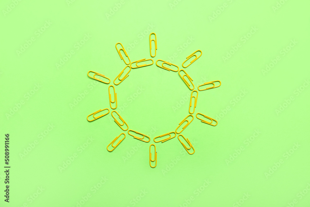 Sun made of yellow paper clips on green background