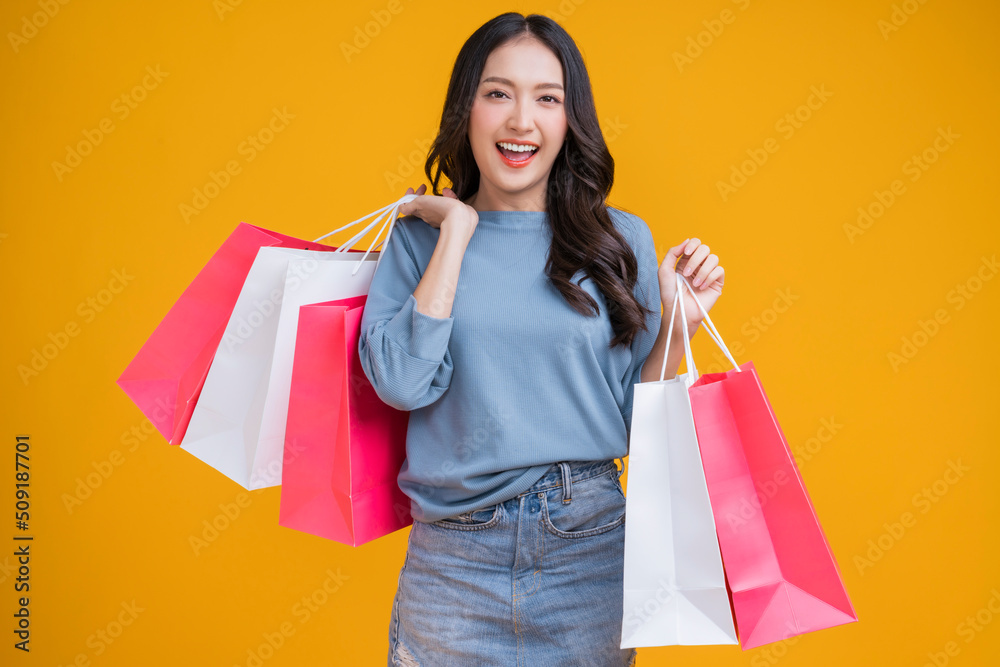 Asian happy female woman girl holds colourful shopping packages   standing on yellow background stud