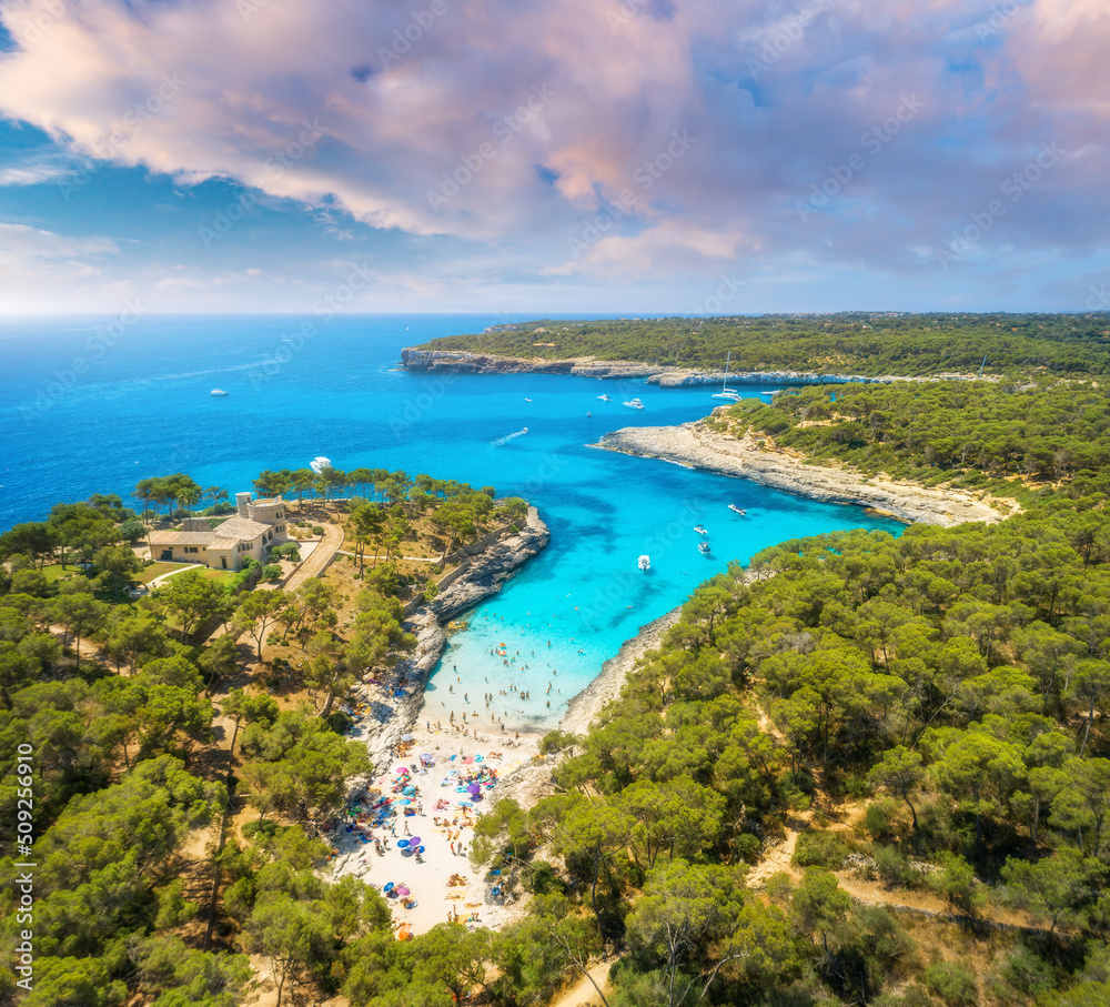 Aerial view of sandy beach with colorful umbrellas, green forest, swimming people in sea bay with cl