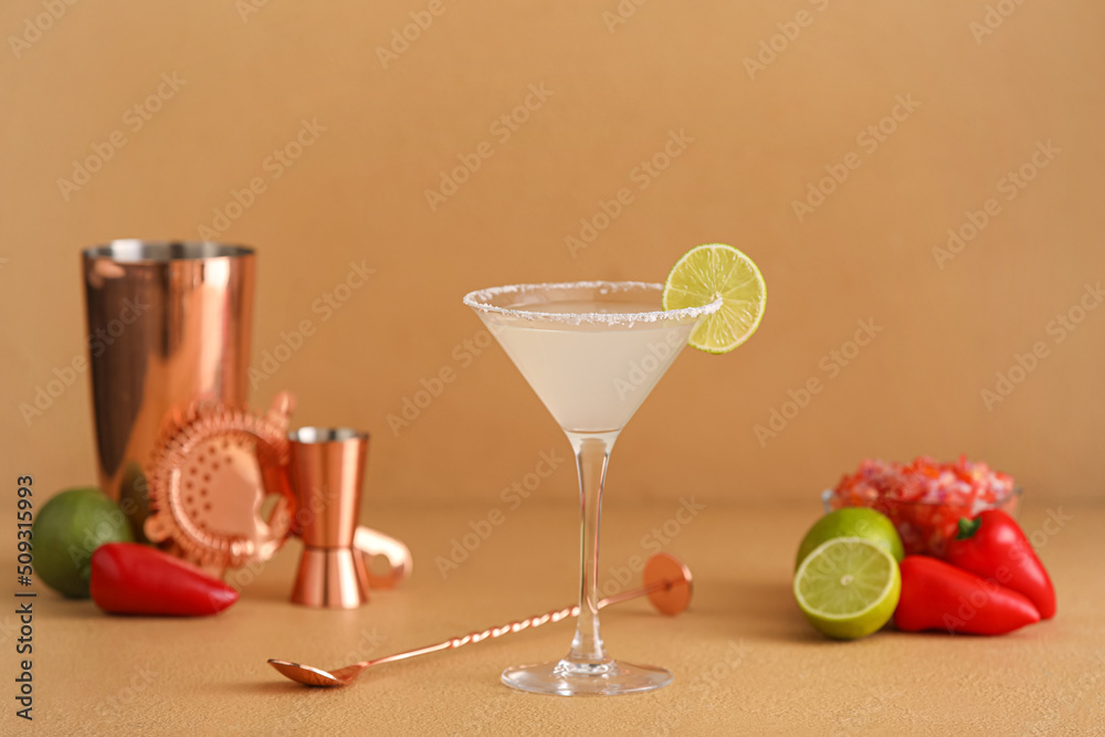 Glass of tasty margarita cocktail with shaker, lime and jalapeno on color background