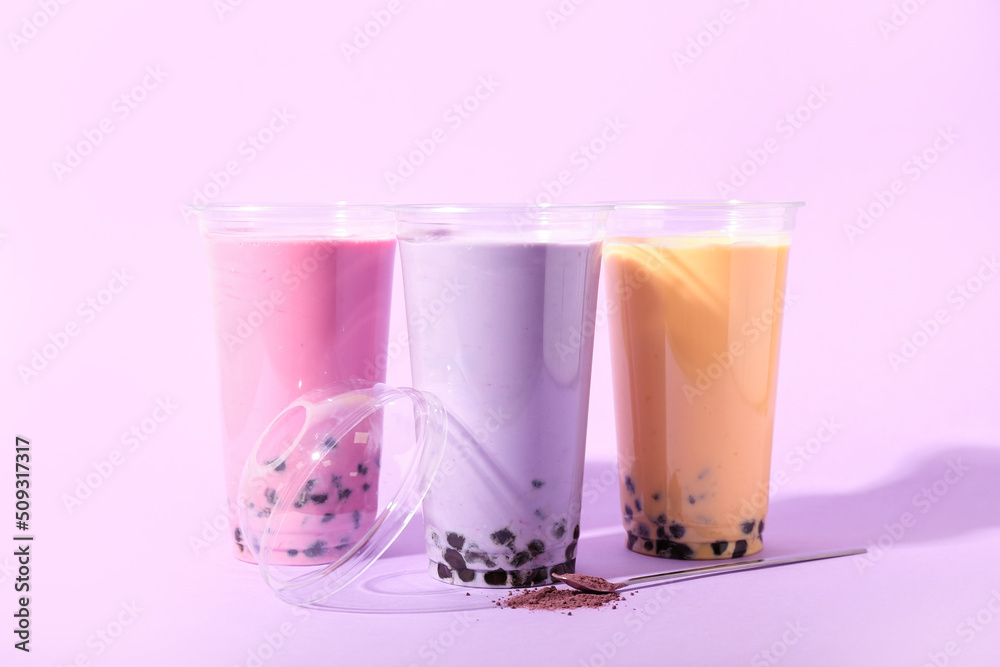 Plastic cups of different tasty bubble tea on purple background