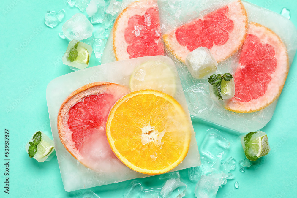 Fresh slices of citrus fruits frozen in ice on turquoise background