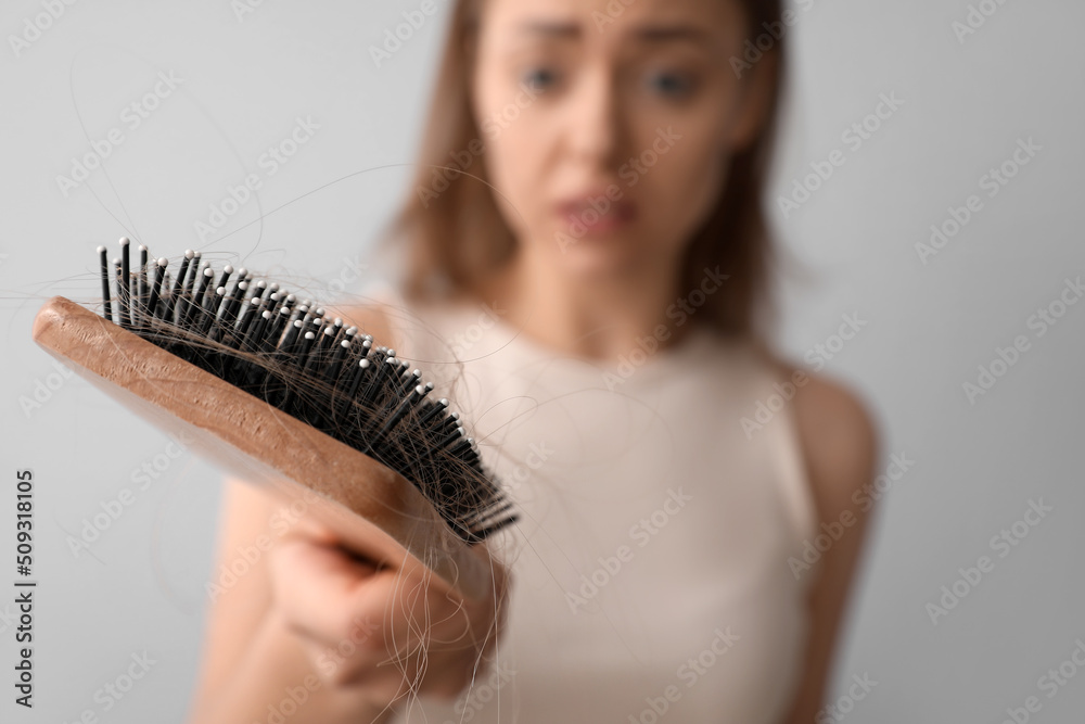 有脱发问题的年轻女子拿着刷子在浅色背景下特写