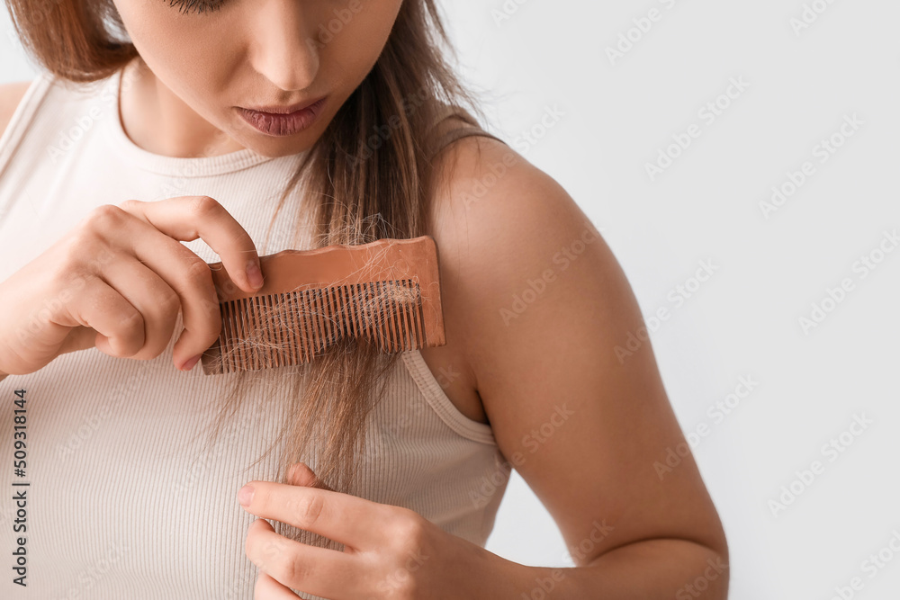 Young woman with hair loss problem on light background