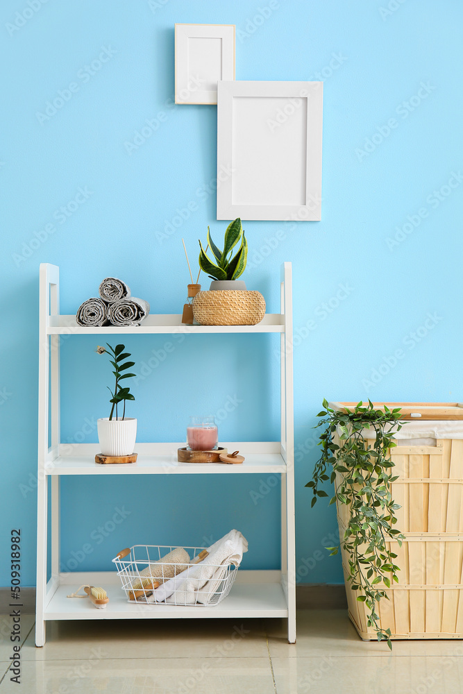 Shelving unit with bath supplies and laundry basket near blue wall