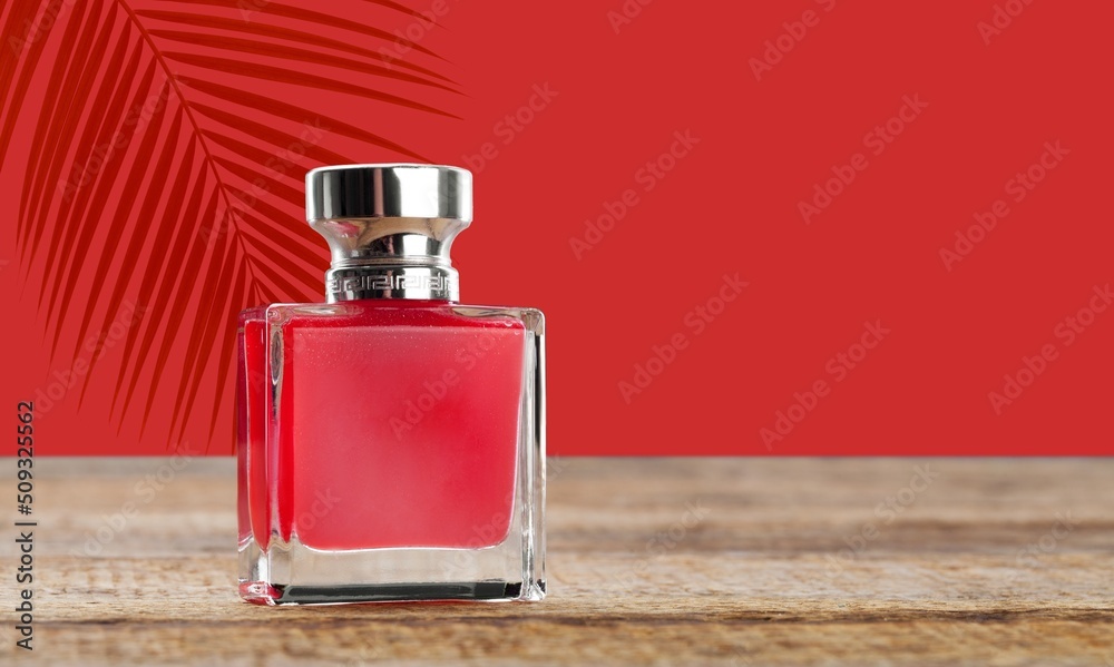 Bottle of perfume on a red background with palm leaves shadow.