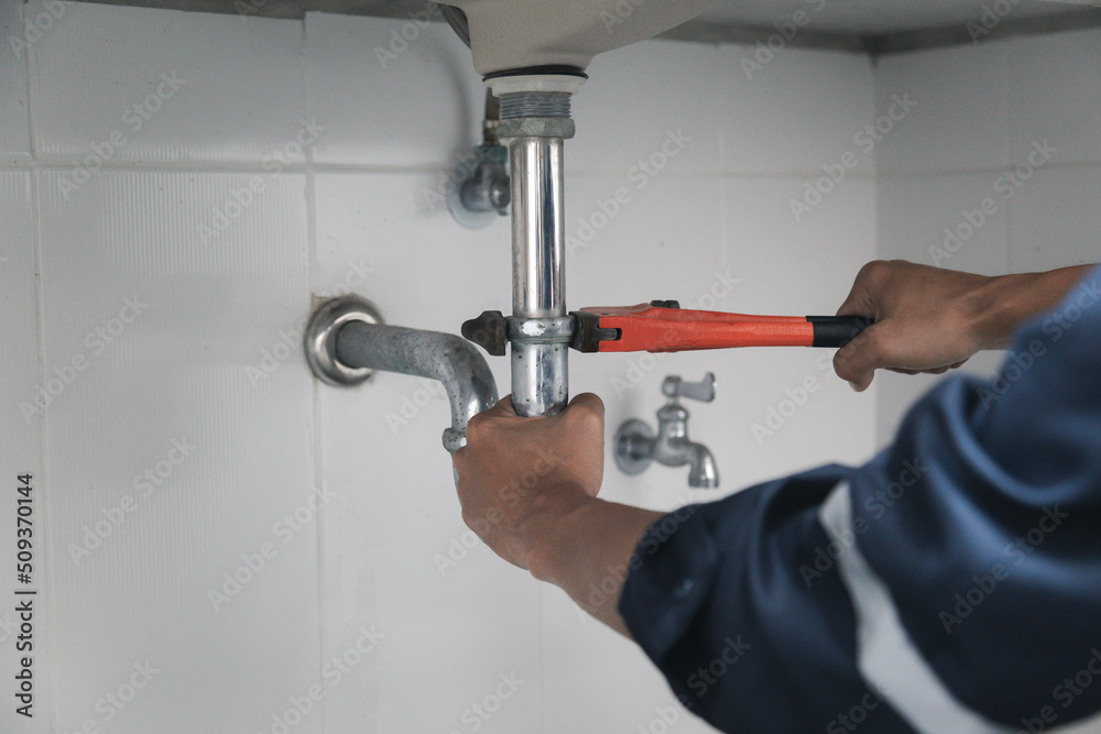 Male Plumber Using Wrench To Fix Leaking Sink In Home Bathroom.