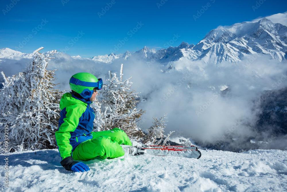 滑雪男孩坐在被云层覆盖的山顶上看