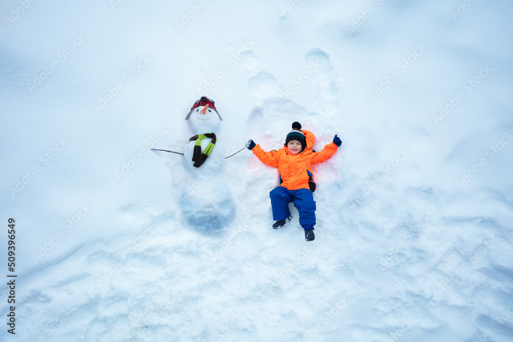 Boy in sport winter orange coat lay holding hand of snowman