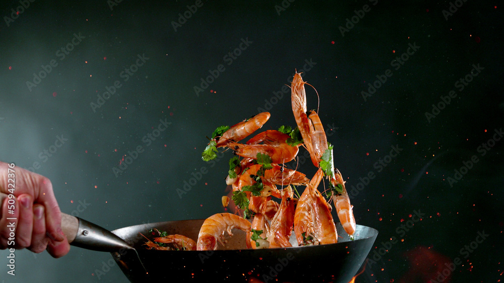 Closeup of chef throwing shrimps from wok pan in fire.