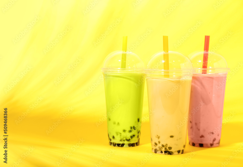 Plastic cups of different tasty bubble tea on yellow background