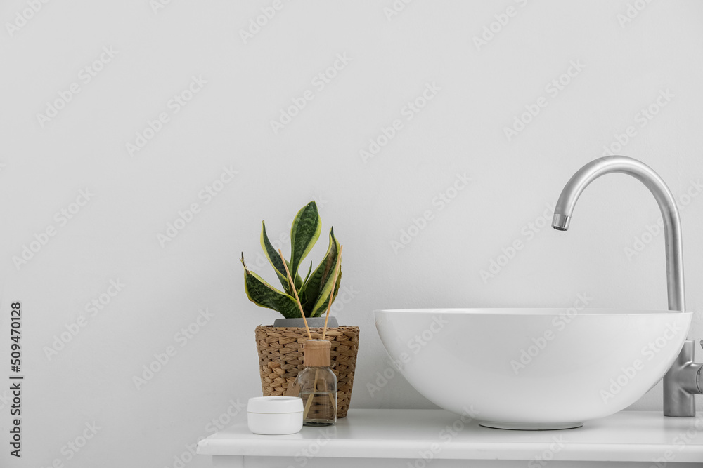 Table with sink, houseplant, jar of cream and reed diffuser near light wall