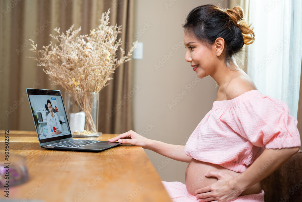 Asian attractive pregnant woman video call with doctor in living room.