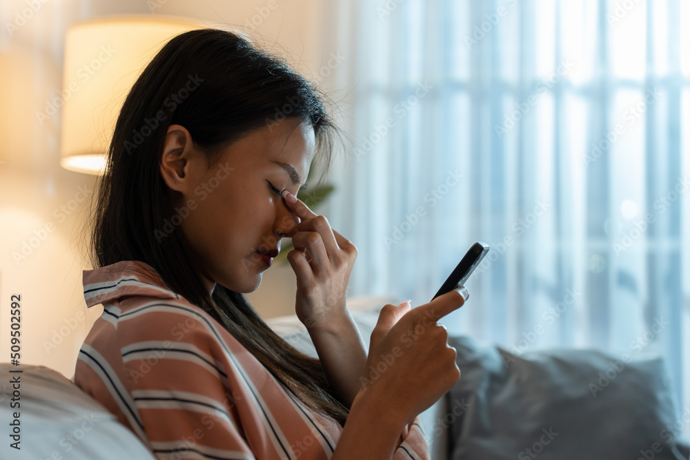 精疲力竭的亚洲年轻女子晚上使用手机时伤到了眼睛