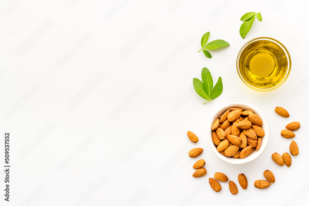 Sweet almond oil in glass jar and almond seeds with green leaf