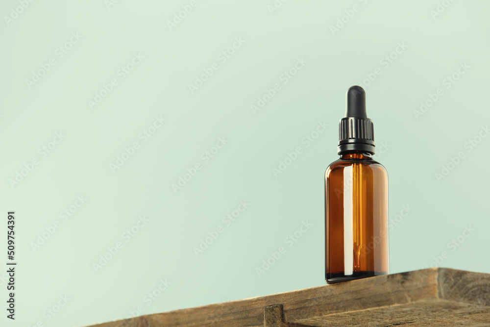 Amber glass dropper bottle and cherry blossom flower on wood shelf, green background. Skincare produ